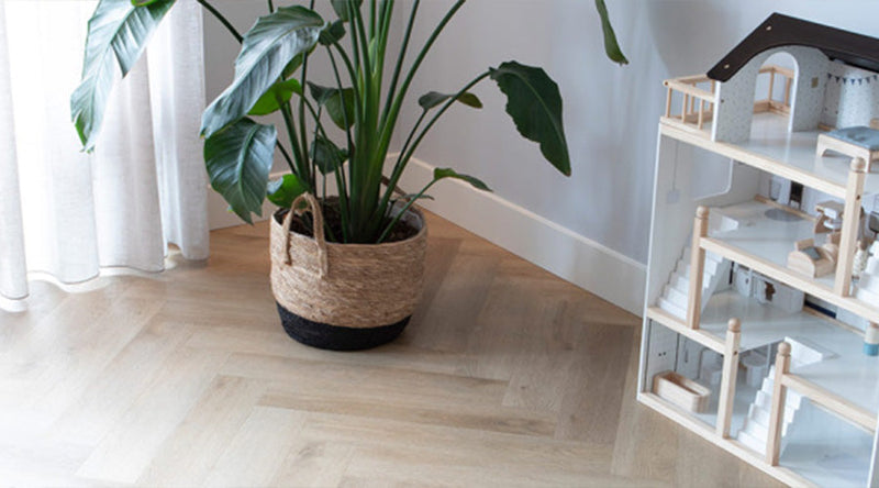 Lichte visgraat vloer in een sfeervolle woonruimte met planten en natuurlijke materialen, zorgt voor een rustige en warme uitstraling.