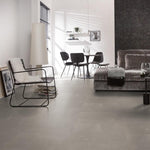 lichte vloer met grote tegels in asgrijs met subtiel golvend streeppatroon, moderne woonkamer met metalen frame stoel en grijze velvet bank