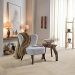 lichte beige eiken vloer met visgraatpatroon en brede planken in een warme, natuurlijke woonkamer met een lichtgrijze fauteuil, een grofgebreide beige plaid en een houten bijzettafel met organische vormen