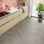Lichtgrijze vloer met visgraatpatroon en subtiele houtstructuur in moderne keuken met beige keukenkasten en roze geglazuurde wandtegels.