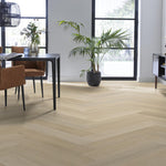 licht eiken vloer met visgraat patroon, brede planken met subtiele houtstructuur, moderne lichte woonkamer met zwart metalen tafel en cognac kleurige stoelen