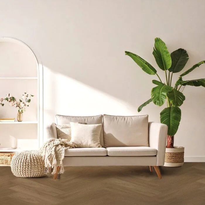 lichte houtkleurige vloer in visgraatpatroon met brede planken, gecombineerd met een beige bank, natuurkleurige gebreide poef en grote kamerplant in moderne, lichte woonkamer