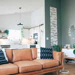 lichtbruine vloer met brede planken in rechte houten structuur in een moderne woonkamer met cognac kleurige leren bank en witte keuken op de achtergrond