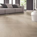 lichte beige eiken visgraatvloer met subtiele houtnerfstructuur in moderne woonkamer met grijze stoffen bank en grote ramen