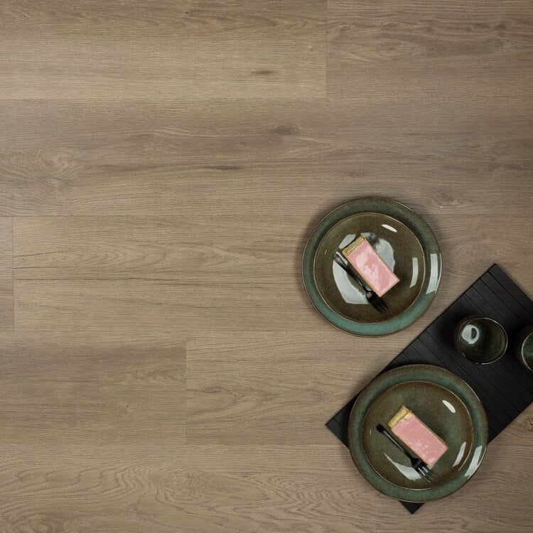 lichte beige eiken vloer met brede planken en subtiele houtnerfstructuur met twee groene borden met stukjes roze gebak en zwarte besteksets op een zwarte placemat