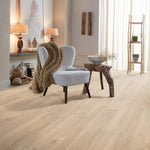 licht beige eiken vloer met brede planken in naturel houtstructuur in een warme, lichte woonkamer met een lichtgrijze stoel en houten bijzettafel