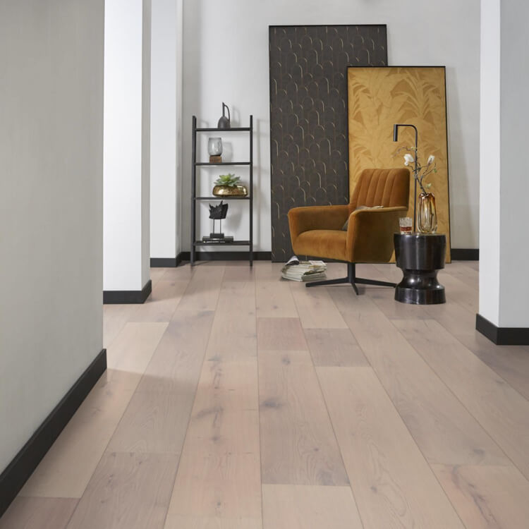 lichte vloer met brede planken in licht wit es kleur met subtiele houtstructuur en natuurlijke noesten, geplaatst in een moderne ruimte met okerbruine stoffen fauteuil en zwarte decoratieve elementen