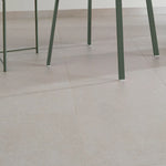beige tegelvloer met grote vierkante tegels en subtiele vlekstructuur onder groene metalen stoelen