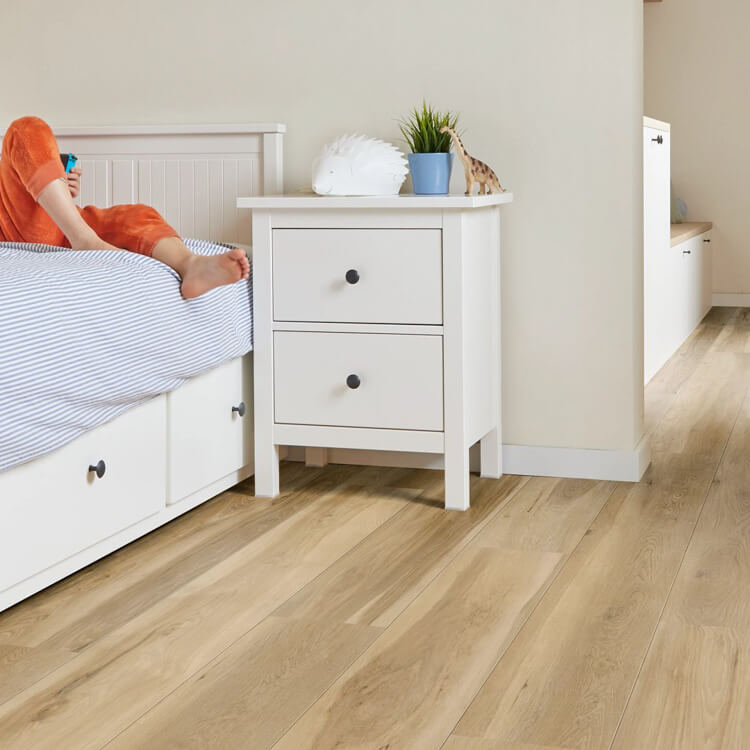 lichte eiken houten vloer met brede planken in een slaapkamer naast een wit nachtkastje met twee lades en een blauw bloempotje met een plant erop