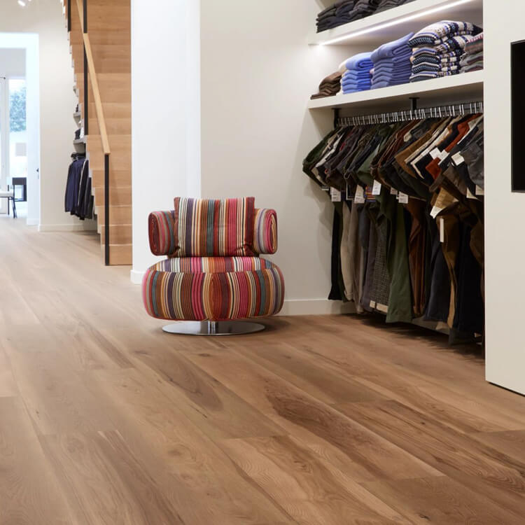 lichte bruin eiken vloer met brede planken en een natuurlijke houtstructuur in een moderne winkelruimte met kleurrijke gestreepte fauteuil en kledingrekken aan de muur