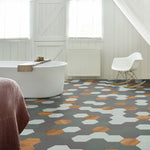 Hexagonvormige vloer met patroon van grote zeshoekige tegels in donkergrijs, lichtgrijs en warm bruin eiken, in moderne badkamer met vrijstaand wit bad en witte schommelstoel.