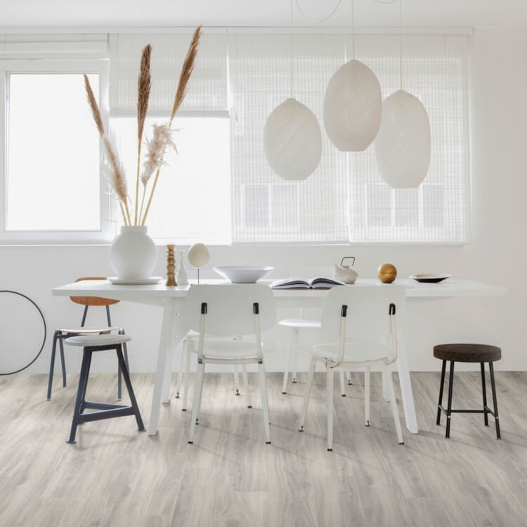 lichte vloer met brede planken in licht wit eiken kleur met subtiele nerfstructuur, moderne witte eetkamertafel met zes stoelen en drie grote witte hanglampen, minimalistisch interieur met natuurlijke accessoires en veel daglicht