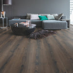 Donker bruin eiken vloer met brede planken en natuurlijke houtstructuur in moderne woonkamer met grijze hoekbank en zwarte ronde salontafel.
