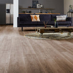 lichte beige eiken vloer met subtiele houtstructuur en brede planken in moderne woonkamer met donkerblauwe bank en industrieel pallet salontafel op ronde beige vloerkleed