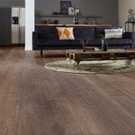 donker grijs bruin vloer met brede planken en zichtbare houtnerf structuur in woonkamer met donkerblauwe bank en houten salontafel op wielen met rond beige blauw vloerkleed