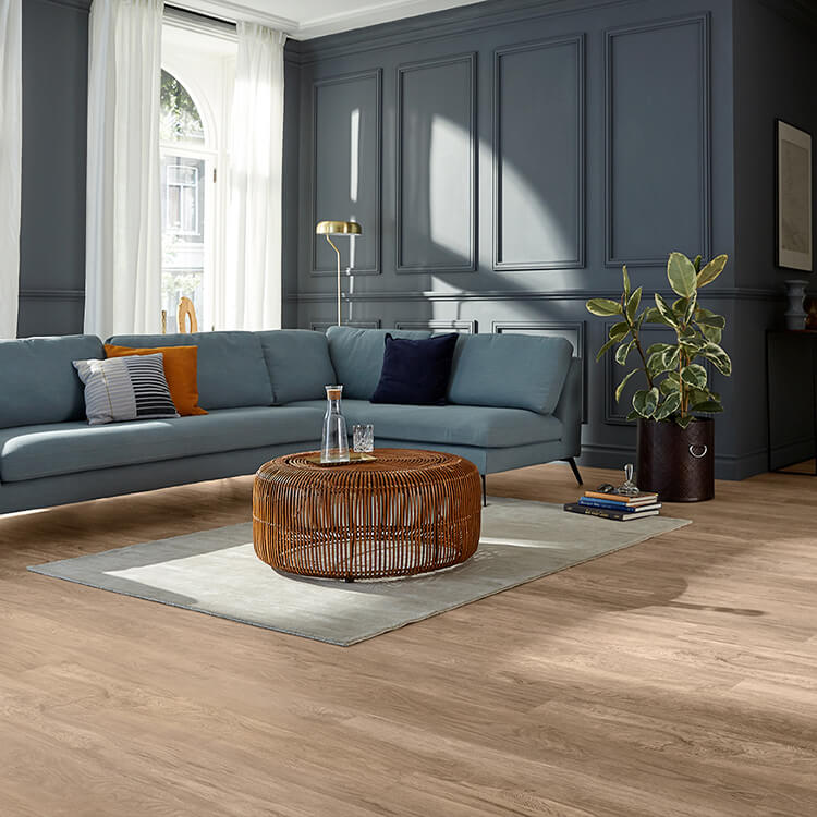 lichte eiken vloer met natuurlijke houtstructuur en brede planken in een moderne woonkamer met antracietgrijze wandpanelen en een lichtgrijs vloerkleed onder een rotan salontafel