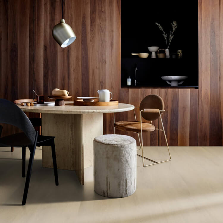 lichte beige vloer met subtiele structuur, eenvoudige effen afwerking in moderne eetkamer met ronde licht natuursteen tafel en donkere houten wandbekleding met verticale lamellen