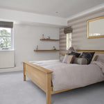 lichte slaapkamer met een effen lichtgrijze vloer en houten bedframe van naturel eikenhout, neutrale muren met horizontale beige strepen en eenvoudige houten wandplanken