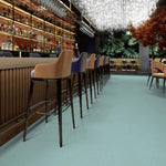 licht egaal turquoise vloer met zachte structuur in moderne baromgeving met hoge barkrukken in beige en blauw, glazen wand met groene plantenprint en sfeerverlichting aan plafond