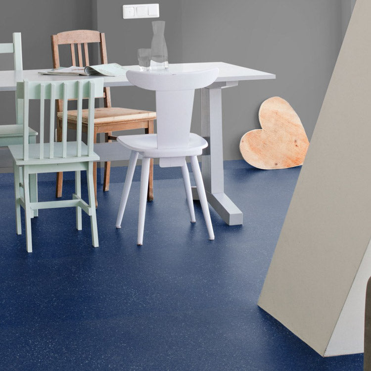 Donkerblauwe vloer met fijne lichte korrelstructuur, gecombineerd met lichte houten stoelen en wit tafelblad in een moderne lichte ruimte.