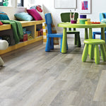 Lichte grijs eiken vloer met rechte planken en subtiele houtnerfstructuur in een kinderkamer met kleurrijke kinderstoelen en een ronde groene tafel.