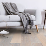 licht beige eiken vloer met brede planken en zichtbare houtnerf in een moderne woonkamer met grijze bank en grijs geruite deken