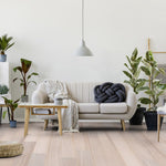 lichte eiken vloer met brede planken in rechte houtnerf, moderne woonkamer met beige stoffen bank, houten salontafel, zwarte knoopvormige sierkussen en verschillende groene planten
