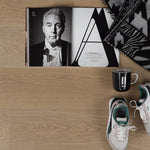 lichte laminaatvloer in eikenstructuur met fijne houtnerf en subtiele beige tint, met opengevouwen zwart-wit magazine, zwart-witte geprint deken, zwarte mok met witte tekst en wit-groene sneakers op de vloer geplaatst