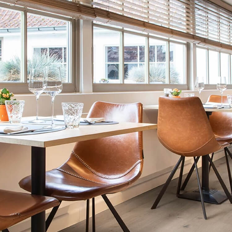 licht eiken vloer met brede planken in houtpatroon onder een moderne eetruimte met cognackleurige leren stoelen en glazen servies op witte tafels naast grote ramen