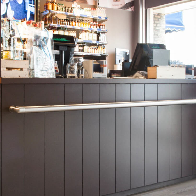 donkergrijze verticale lamellenwand met matte structuur en glad roestvrijstalen leuning in moderne horecaomgeving met barkassa en glazen opstelling