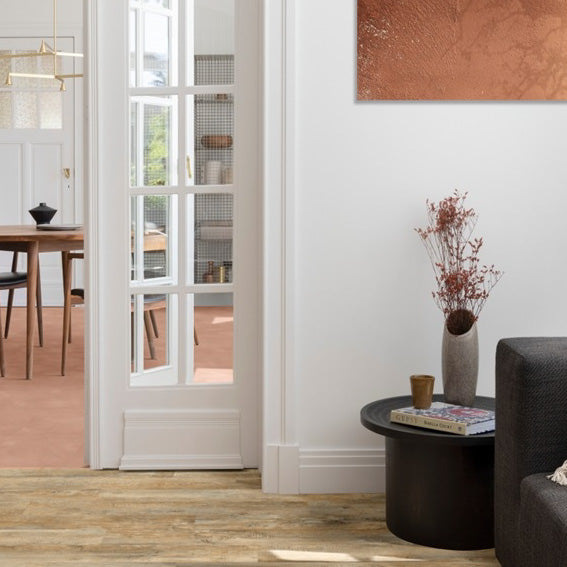 lichte beige eiken vloer met brede planken en natuurlijke houtstructuur in moderne woonkamer met zwarte salontafel en witte deur naar aangrenzende ruimte met terracotta tegelvloer