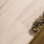 lichte beige eiken vloer met subtiele houtstructuur en brede planken, deels bedekt door een mat met blauwe en gele franjes zichtbaar aan de rechterkant