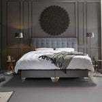 donkergrijze vloer met effen structuur in slaapkamer, combinatie met grijs gestoffeerd bed, wit beddengoed en aangesloten donkergrijze wand met decoratief rond reliëfpaneel