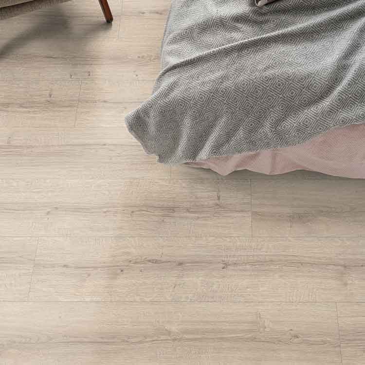 licht beige eiken vloer met subtiele houtnerfstructuur en lange smalle planken naast een bed met grijs deken met geometrisch patroon