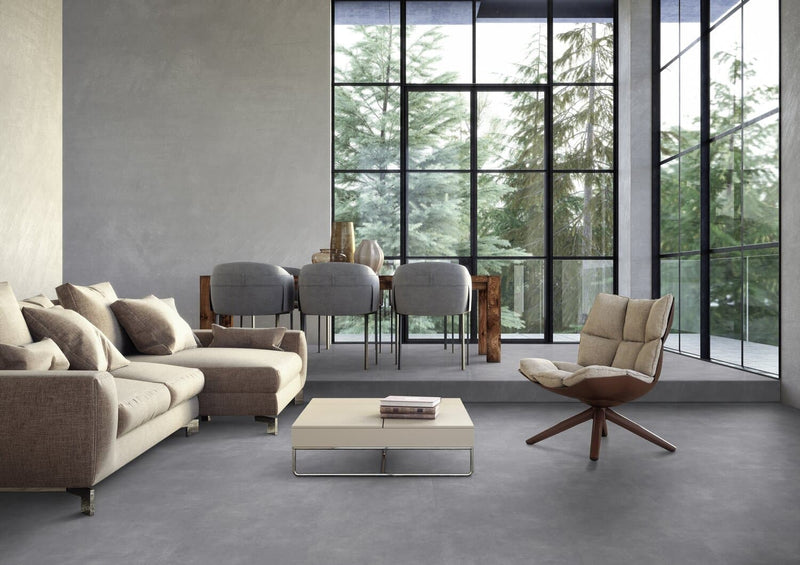 donkergrijze tegelvloer met grote, matte tegels en een subtiel golvend streeppatroon in een moderne woonkamer met beige stoffen hoekbank, beige draaifauteuil en houten eettafel met grijze stoelen voor grote raampartijen
