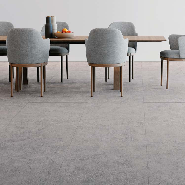 Tegelvloer met grote tegels in licht grijs betonstructuur, moderne eetkamer met grijze gestoffeerde stoelen en houten tafelpoten.