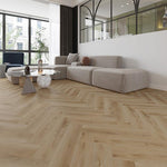 licht eiken vloer in visgraat patroon met subtiele noesten en natuurlijke houtstructuur, gecombineerd met modern grijs beige hoekbank en glazen salontafel met marmeren voet in lichte, ruime woonkamer met veel natuurlijk licht