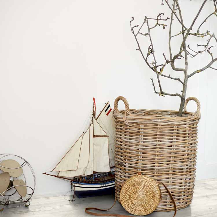 lichte beige eiken houten vloer met subtiel zichtbare nerfstructuur, witte muur op de achtergrond, een gevlochten rotan mand met een kale tak en een rond gevlochten tasje ernaast, daarnaast een vintage metalen ventilator en een houten modelboot met witte zeilen