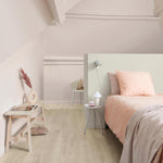 lichte vloer met brede planken in licht eiken houtpatroon, slaapkamer met zachtroze beddengoed, pastelgroene scheidingswand en minimalistische houten details