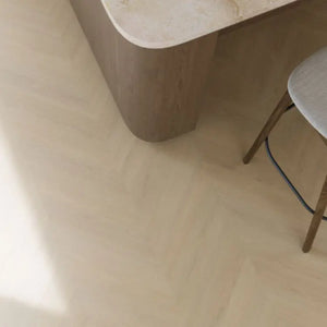 lichte beige eiken vloer in visgraatpatroon met matte afwerking, hoek van een houten meubel en stoel met lichtgrijze stoffering zichtbaar
