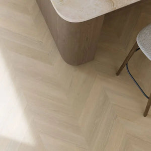 lichte beige eiken vloer met visgraatpatroon en subtiele houtstructuur, gecombineerd met afgeronde houten meubelrand en stoelpoten in warm bruin houtkleur