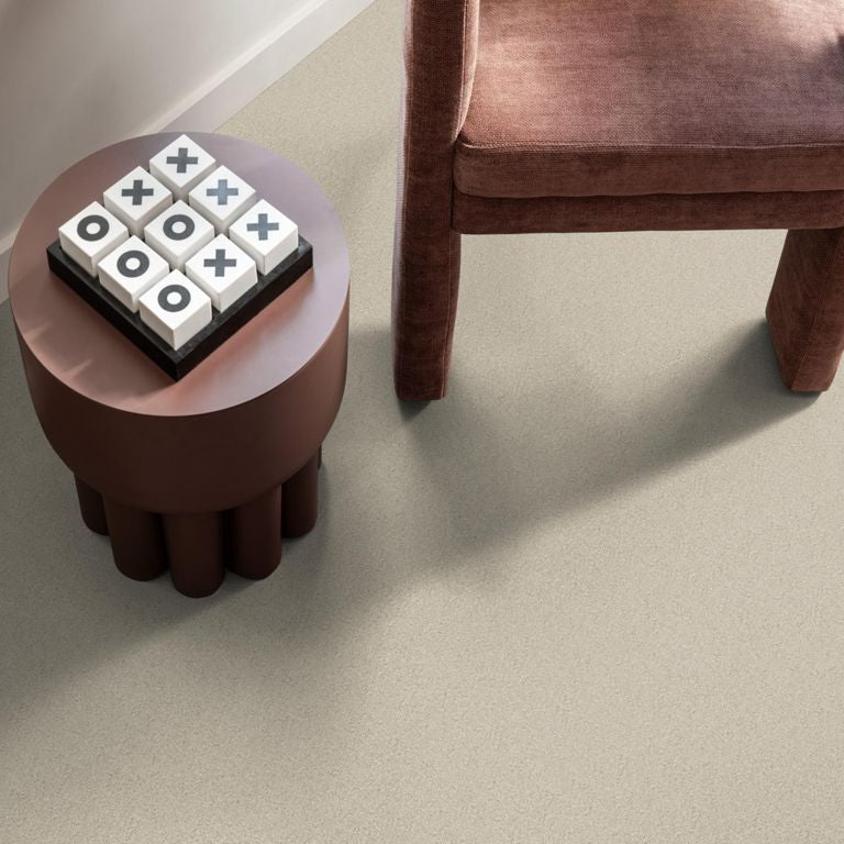 licht taupe gekleurde vloer met fijne, subtiele grindstructuur, gecombineerd met donkerbruine stoffen stoel en rond tafeltje met groot kruis-en-rondjes spel