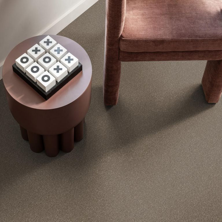 licht taupe kleurige vloer met fijne korrelige structuur, zachte matte afwerking naast donkerroze velours fauteuil en bijzettafel met spelletje kruisjes en rondjes