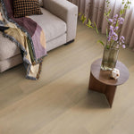 licht beige eiken vloer met brede planken en zachte nerfstructuur in een woonkamer met beige bank en houten bijzettafel met vaas en bloemen