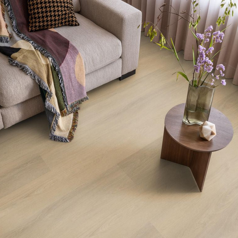 lichte beige eiken vloer met brede planken, subtiel houtnerfstructuur, gecombineerd met een beige stoffen bank en een houten bijzettafel met vaas en paarse bloemen