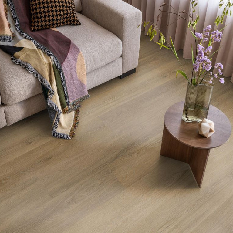 licht beige eiken vloer met brede planken en subtiele houtnerfstructuur in modern interieur naast beige bank met kleurrijk geweven plaid en klein rond houten tafel met vaas en bloemen