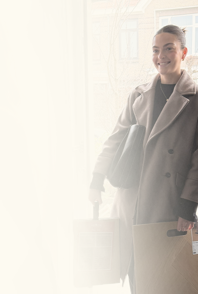 vrouw met beige mantel en zwarte tas die twee dozen met vloerbedekking vasthoudt voor een lichte achtergrond