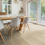 lichte vloer in brede planken met een subtiele houtstructuur in licht eiken kleur, gecombineerd met een moderne eetkamer met witte stoelen en veel natuurlijk licht vanuit grote ramen