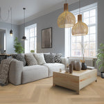 lichte vloer in visgraat patroon met brede planken in licht eiken, moderne zithoek met grijs stoffen hoekbank, houten salontafel en zwarte en witte kussens met abstract geometrisch patroon