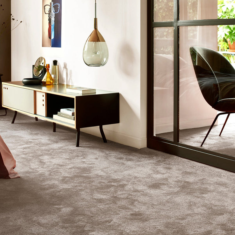 Zacht taupekleurig tapijt met lichte, pluizige structuur in een moderne, lichte woonkamer met zwarte metalen kozijnen en een minimalistisch houten dressoir met decoratieve objecten.